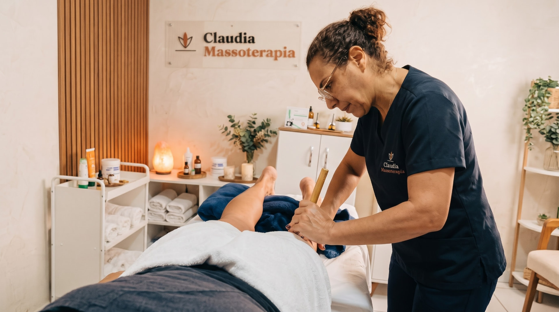 Claudia atendendo uma cliente na maca, com bastão de bambu, na sala da Claudia Massoterapia